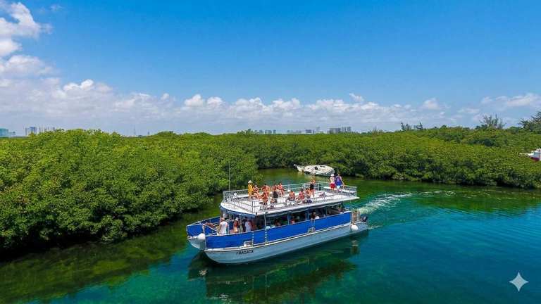 Two-story Fragata catamaran cruising a clear mangrove channel in Cancun with guests on the upper deck during the shared tour to Isla Mujeres.