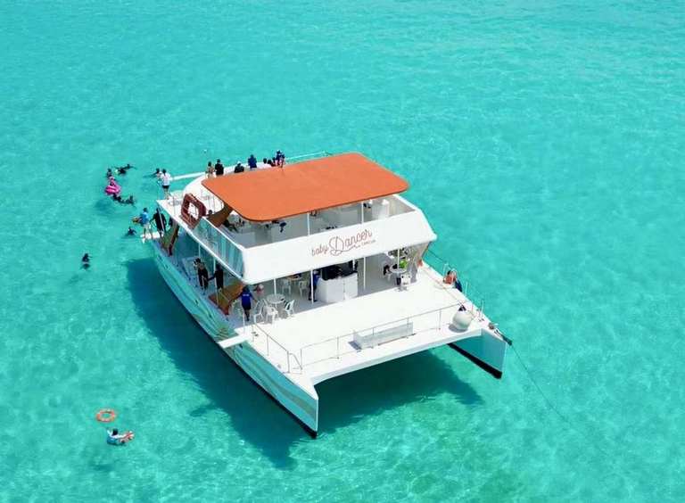 Aerial view of 60 ft MiniDancer catamaran anchored on turquoise Caribbean reef near Isla Mujeres with snorkelers around for group charter rental.