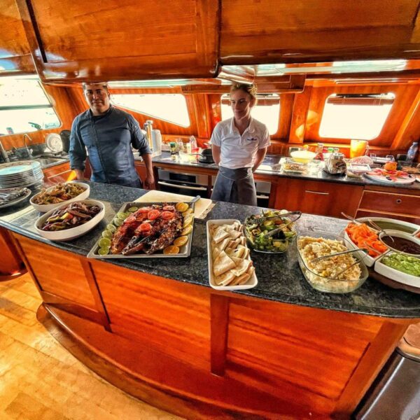 Chef privado y miembro de la tripulaci&oacute;n detr&aacute;s de la barra de la cocina del yate cargada de costillas asadas, fajitas, wraps y ensaladas frescas a bordo.