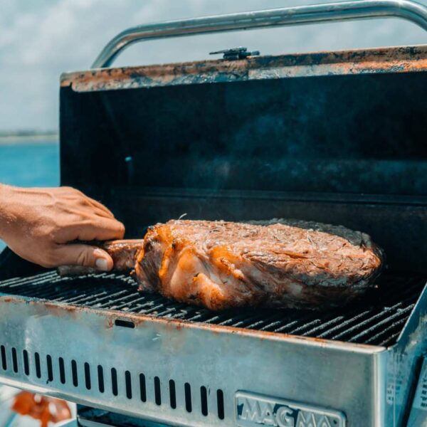 Mano volteando un tomahawk sazonado en una parrilla Magma de acero inoxidable montada a bordo sobre el Caribe azul.
