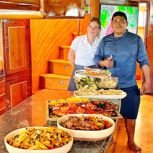 Chef alegre y tripulaci&oacute;n posando junto a una presentaci&oacute;n en niveles de fajitas, pescado asado, pasta y ensaladas a bordo del yate.