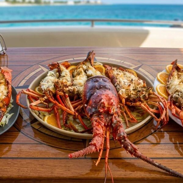 Tres platos de colas de langosta a la parrilla con c&iacute;tricos servidos en una mesa de teca del yate junto al Caribe turquesa.