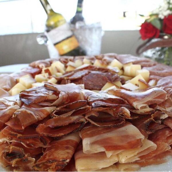 Generosa tabla circular de charcuter&iacute;a con jamones curados, salami y quesos servida con vino fr&iacute;o a bordo.