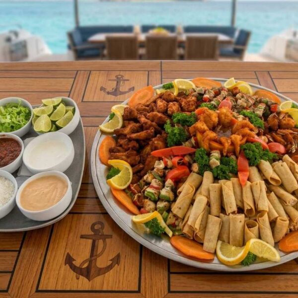Gran plat&oacute;n de catering con camarones capeados, taquitos y brochetas de pollo con salsas de acompa&ntilde;amiento en un yate anclado.