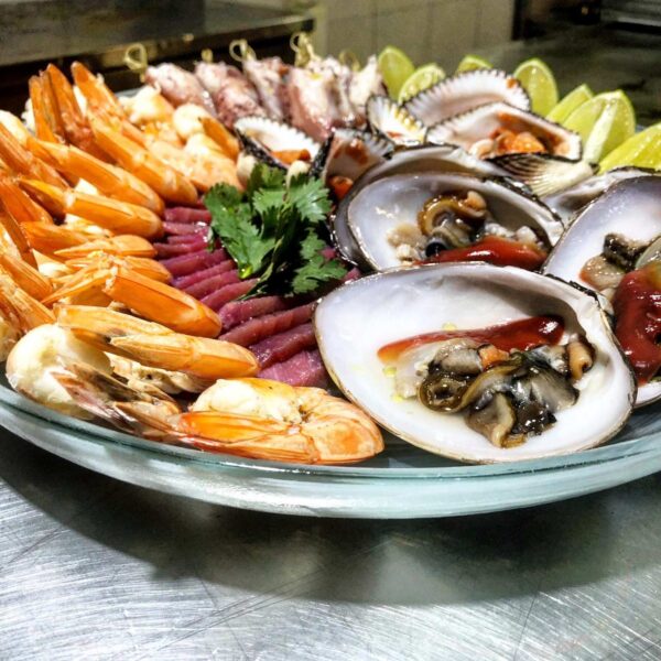 Plat&oacute;n de mariscos frescos con camar&oacute;n, ostras crudas, at&uacute;n y lim&oacute;n dispuestos en un plato de vidrio en la cocina.