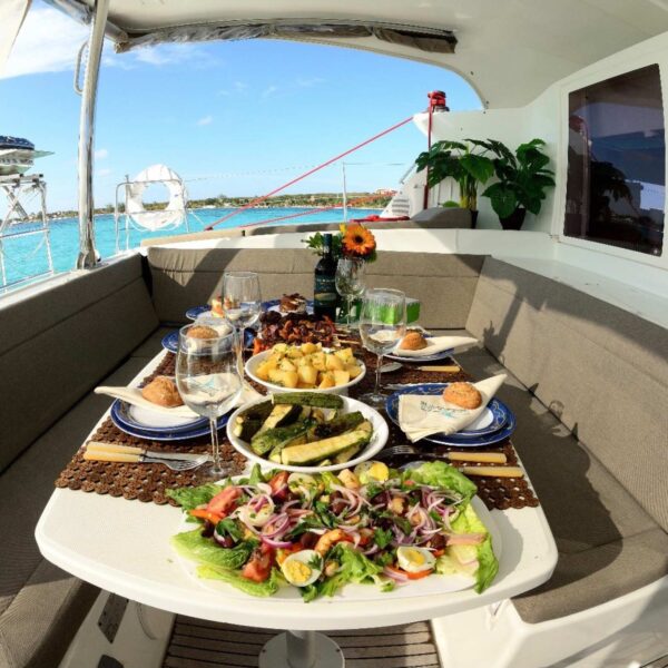 Mesa en la ba&ntilde;era del catamar&aacute;n servida con ensalada verde, calabacita a la parrilla, papas rostizadas y vino junto al Caribe.