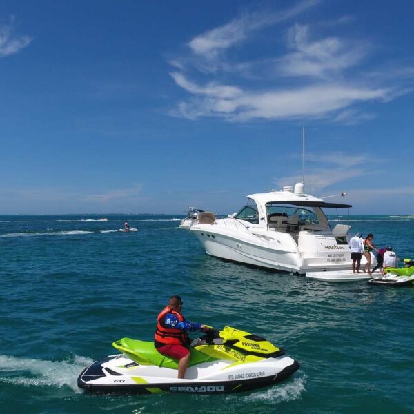 Piloto de jet ski Sea-Doo pasando r&aacute;pido junto a un yate anclado y una segunda wave runner durante una aventura en charter privado en Canc&uacute;n.