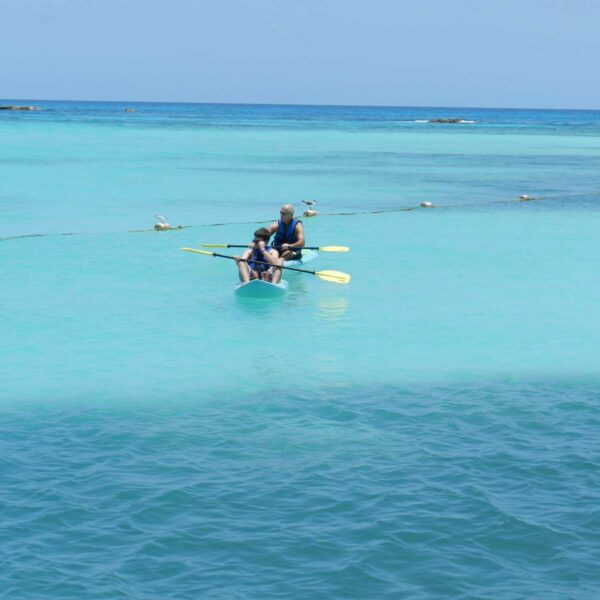 Pareja remando en un kayak transparente por aguas turquesas calmas del Caribe cerca de Canc&uacute;n en un tour relajado de yate.