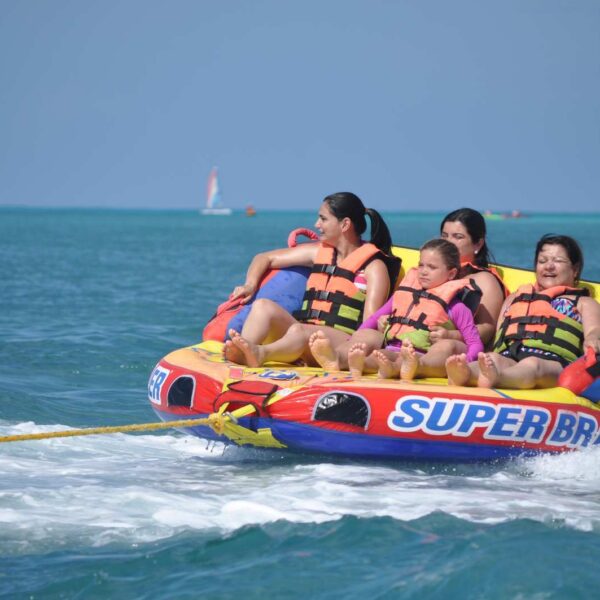 Familia con chalecos salvavidas montada en el remolcable inflable Super Brain, salpicando por el Caribe detr&aacute;s de un barco de Canc&uacute;n.