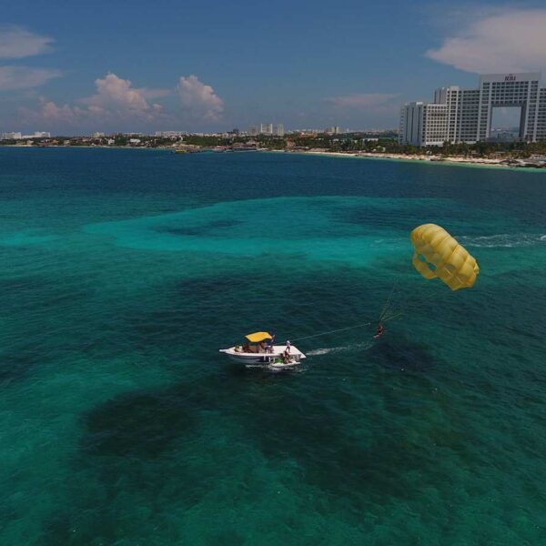 Vista a&eacute;rea de una lancha de parasailing arrastrando un paraca&iacute;das amarillo sobre las aguas del arrecife frente a las playas de la zona hotelera de Canc&uacute;n.