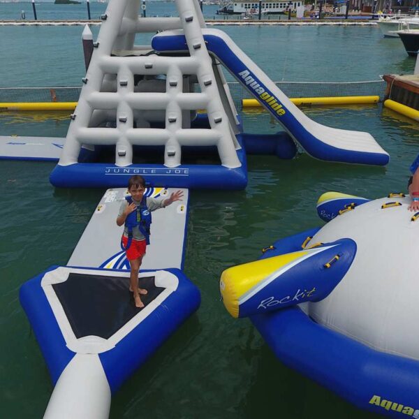 Ni&ntilde;os con chalecos salvavidas jugando en un parque acu&aacute;tico inflable flotante Aquaglide con torre de escalada, tobog&aacute;n y brincol&iacute;n en Canc&uacute;n.