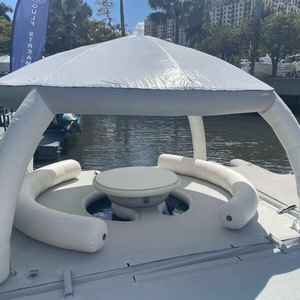 Inflatable AquaBanas cabana with shaded dome roof and cushioned U-shaped seating around a central table, displayed at a Florida boat show.