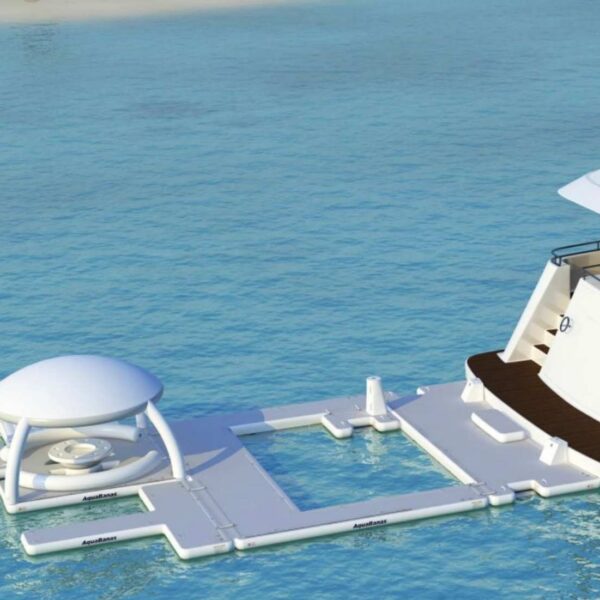 AquaBanas inflatable floating pool platform attached to a luxury yacht's swim deck, enclosing a sea-water swimming area beside a shaded cabana.