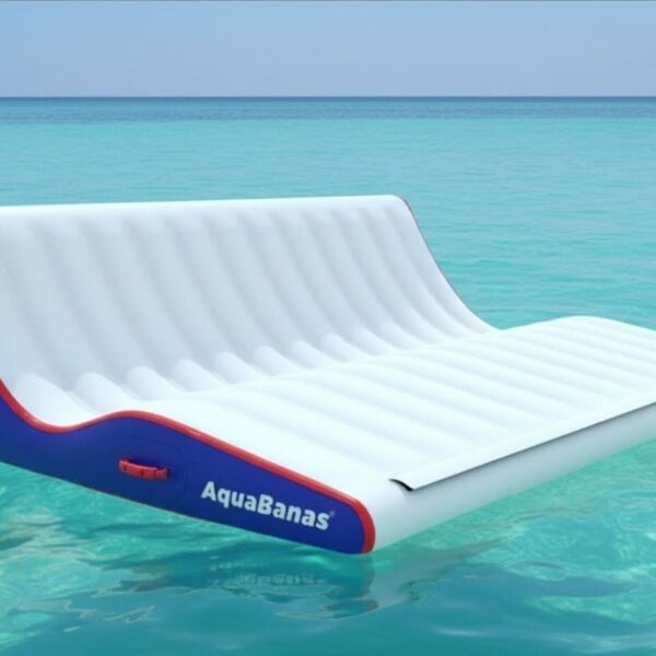 AquaBanas inflatable double chaise lounge with blue and red trim floating on glassy turquoise Caribbean water, perfect for two guests to relax on board.