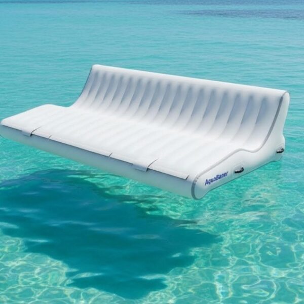 Wide inflatable AquaBanas double sun lounger floating on shallow turquoise Caribbean water for two-person relaxation alongside a private yacht charter.